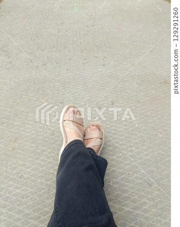 A person in sandals calmly resting their feet on textured pavement 129291260
