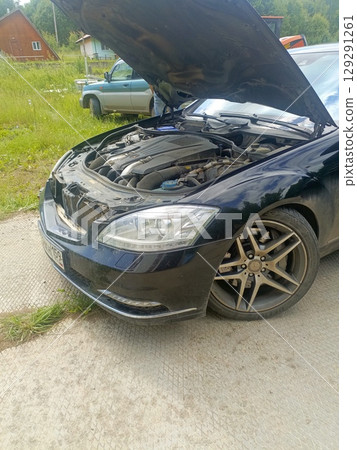 Black luxury car with an open hood representing engine trouble or maintenance 129291261