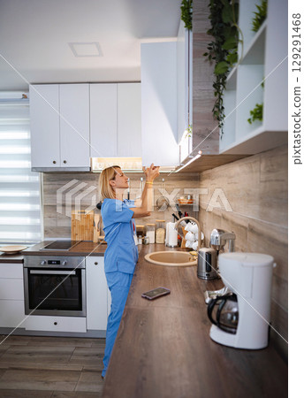 Female Doctor Opening Kitchen Cabinet at Home After Work Female Doctor Opening Kitchen Cabinet at Home After Work 129291468