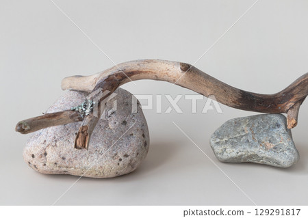 A dry tree branch and stones on a light background. Minimalistic creative composite background for the presentation of cosmetics or products. Front view 129291817