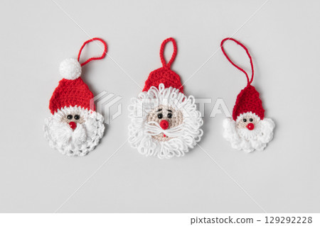Crocheted three toys Santa Claus in a red hat on gray background. Christmas tree decorations. Gift for winter holidays. Top view, flat lay. 129292228