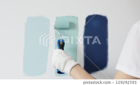 Painter wearing protective gloves rolling blue paint on white wall, creating gradient color effect for home interior renovation project Painter wearing protective gloves rolling blue paint on white wall, creating gradient color effect for home interior renovation project 129292593