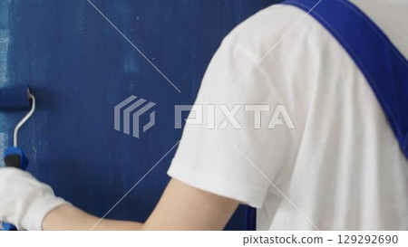 Painter applying blue paint with roller on white wall, showing precise technique and transforming interior space with smooth, even strokes Painter applying blue paint with roller on white wall, showing precise technique and transforming interior space with smooth, even strokes 129292690