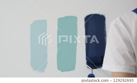Painter wearing protective gloves rolling blue paint on white wall, creating gradient color effect for home interior renovation project 129292693