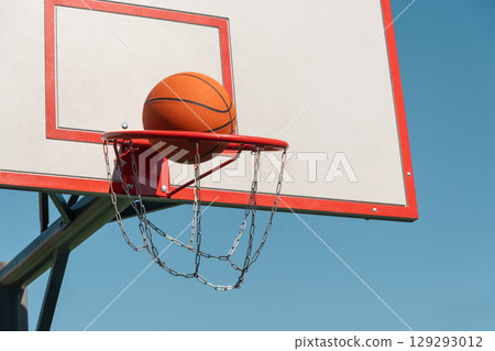 Basketball orange ball in basketball hoop against clear blue sky. Game moment. Outdoors. 129293012