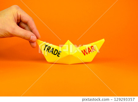 Trade war symbol. Concept word Trade war on beautiful yellow paper boat. Businessman's hand. Beautiful orange paper background. Business trade war concept. Copy space. Trade war symbol. Concept word Trade war on beautiful yellow paper boat. Businessman's hand. Beautiful orange paper background. Business trade war concept. Copy space. 129293357