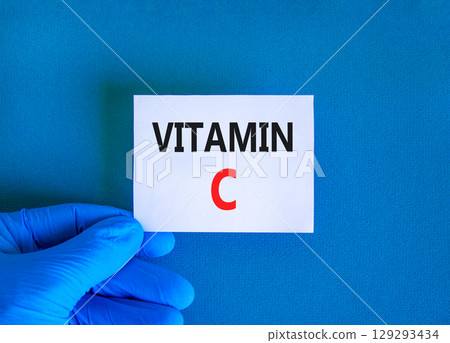 Vitamin C symbol. Concept words Vitamin C on beautiful white card. Doctor's hand in blue medical glove. Beautiful blue background. Medical healthy lifestyle Vitamin C concept. 129293434