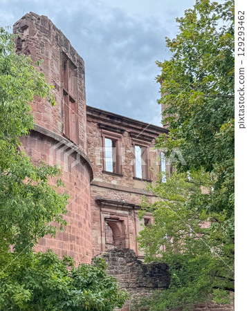 Castle ruins with stone walls and windows stand amidst vibrant trees. The historical architecture harmonizes with lush greenery creating a picturesque scene of ancient heritage and nature Castle ruins with stone walls and windows stand amidst vibrant trees. The historical architecture harmonizes with lush greenery creating a picturesque scene of ancient heritage and nature 129293462