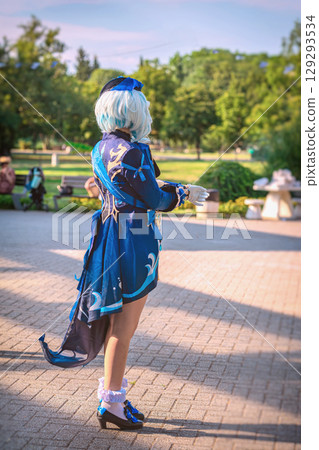Cosplayer woman in detailed blue anime costume with wig and gloves standing outdoors in sunny park. Concept of cosplay character, anime costume, fan culture Cosplayer woman in detailed blue anime costume with wig and gloves standing outdoors in sunny park. Concept of cosplay character, anime costume, fan culture 129293534