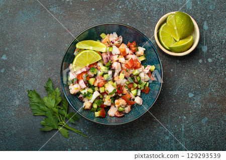 Peruvian seafood ceviche with shrimps, octopus, tomatoes, cucumber, and parsley in a bowl served with lime top view 129293539