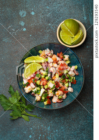 Peruvian seafood ceviche with shrimps, octopus, tomatoes, cucumber, and parsley in a bowl served with lime top view 129293540