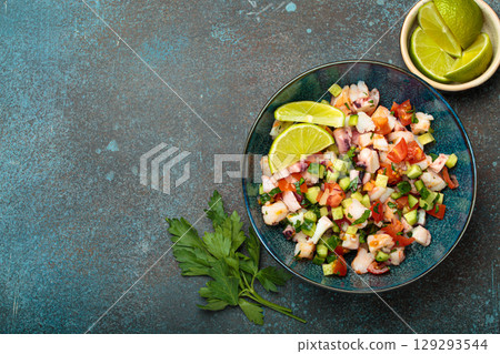 Peruvian seafood ceviche with shrimps, octopus, tomatoes, cucumber, and parsley in a bowl served with lime top view, space for text 129293544