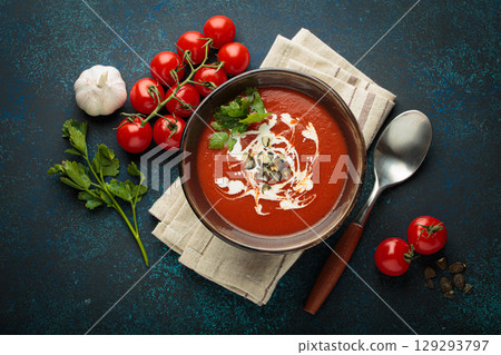 Tomato soup with cream, pumpkin seeds and herbs on blue background top view Tomato soup with cream, pumpkin seeds and herbs on blue background top view 129293797