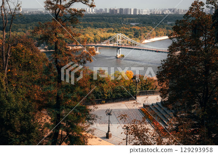 Vintage lamp in autumn Kyiv park overlooks bridge and calm Dnipro waters. 129293958