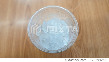 Top View of Ice Cubes in a Transparent Plastic Cup on Wooden Surface Top View of Ice Cubes in a Transparent Plastic Cup on Wooden Surface 129294256