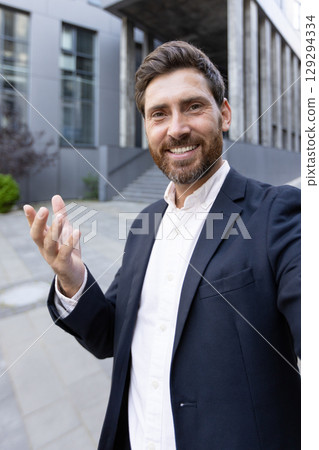 Confident businessman in a formal outfit engaging in a video call outdoors. Captures communication and professionalism in a modern workplace setting. 129294334