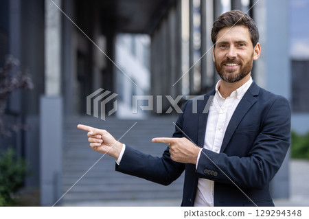 A professional man in business attire presenting or pointing outdoors near modern architecture. Ideal for business, presentation, or success-related projects. 129294348