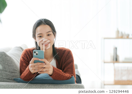 A woman lying on the sofa and using a smartphone A woman lying on the sofa and using a smartphone 129294446