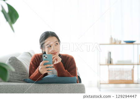 A woman lying on the sofa and using a smartphone A woman lying on the sofa and using a smartphone 129294447