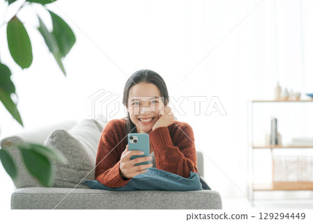 A woman lying on the sofa and using a smartphone A woman lying on the sofa and using a smartphone 129294449