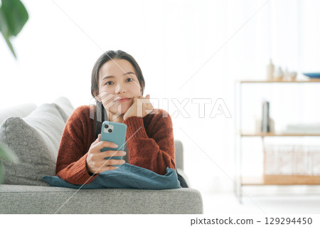 一位女士躺在沙發上使用智慧型手機 129294450