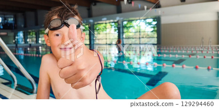 Happy boy giving a thumbs up in an indoor swimming pool. Concept of self-confidence in children's swimming lessons, child development, children's sports Happy boy giving a thumbs up in an indoor swimming pool. Concept of self-confidence in children's swimming lessons, child development, children's sports 129294460