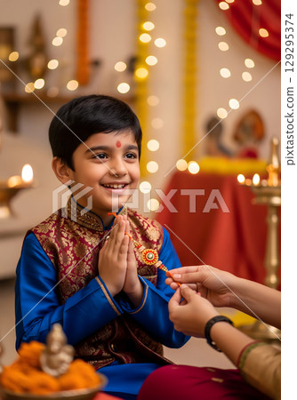 A young Indian boy, approximately seven years old, is shown in prayer with a happy smile while holding a colorful thread bracelet 129295374