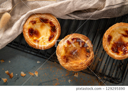 Golden pastel de nata pastries cooling on a black wire rack 129295890