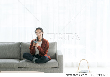 Woman using smartphone on sofa 129299020