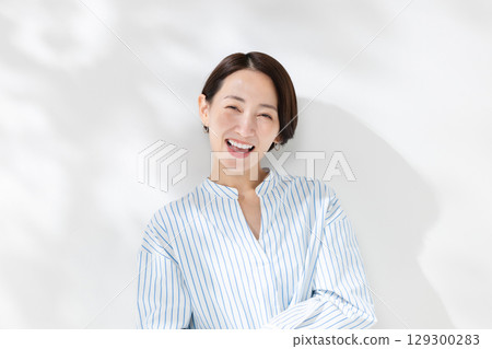 A smiling woman standing in the sunlight filtering through the trees 129300283
