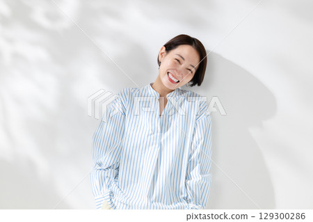 A smiling woman standing in the sunlight filtering through the trees 129300286
