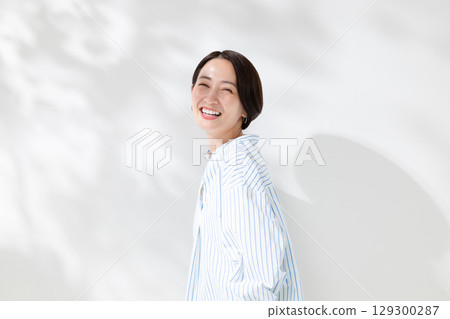 一位微笑的女人站在透過樹梢的陽光下 一位微笑的女人站在透過樹梢的陽光下 129300287