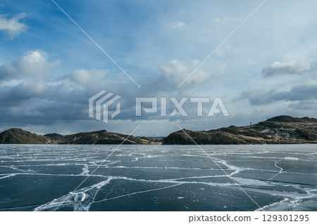 ice-covered lake under cloudy sky with distant hills in background during winter season. ice-covered lake under cloudy sky with distant hills in background during winter season. 129301295