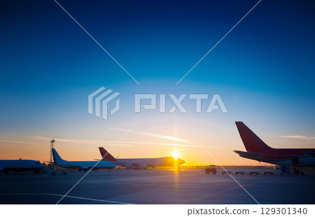 Many planes are standing at the airport at a beautiful sunset. 129301340