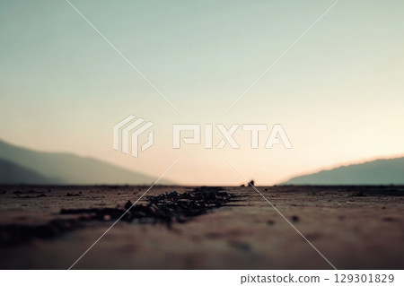 Sunset over a tranquil road with distant mountains and a clear sky creating a serene atmosphere 129301829