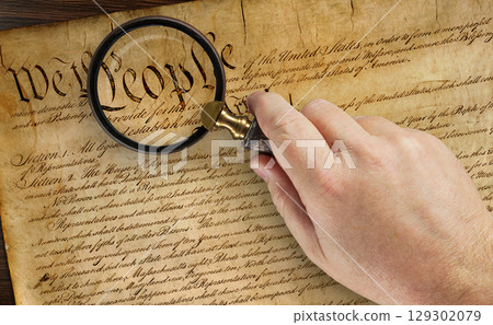 Male Hand Holding Magnifying Glass Over The Work People on the United States Constitution. 129302079