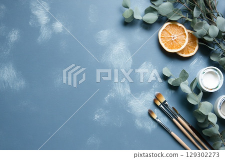 Creative Still Life Paintbrushes, Sliced Orange, and Eucalyptus on a Soft Blue Background 129302273