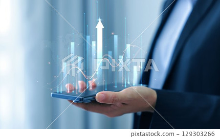 Businessman holding smartphone with glowing stock market chart and upward arrow. Financial growth, investment success, fintech, and trading technology concept. business stock market. Businessman holding smartphone with glowing stock market chart and upward arrow. Financial growth, investment success, fintech, and trading technology concept. business stock market. 129303266