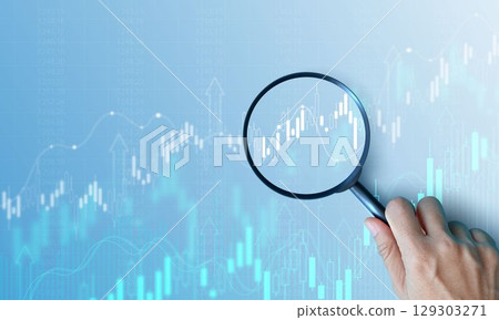 Hand holding magnifying glass analyzing digital financial stock chart. Data analysis, investment research, trading strategy, and financial market concept on blue background. business stock market. 129303271