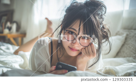 A girl lying face down on the bed looking at her smartphone 129303335
