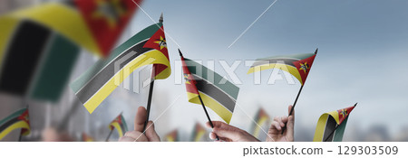 Mozambique flags in their hands on a blurred urban background Mozambique flags in their hands on a blurred urban background 129303509