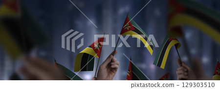 Mozambique flags in their hands on a blurred urban background 129303510