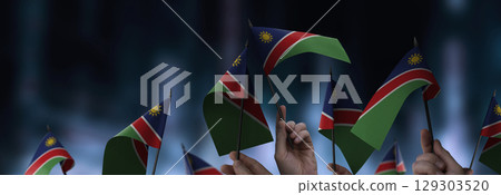 Namibia flags in their hands on a blurred urban background Namibia flags in their hands on a blurred urban background 129303520
