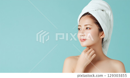 A woman in a towel gently cares for her skin against a blue background 129303855