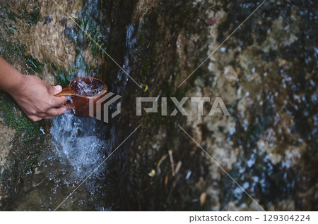 Person Collecting Fresh Water Using a Wooden Cup from a Natural Stream Person Collecting Fresh Water Using a Wooden Cup from a Natural Stream 129304224