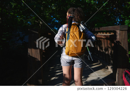 Hiker With Yellow Backpack Crossing a Wooden Bridge in a Forest 129304226