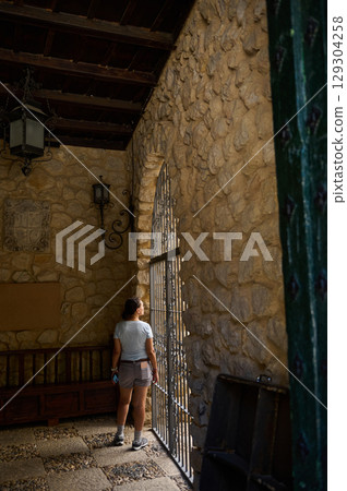 Woman Standing by Stone Architectural Window Viewing Sunlit Exterior 129304258