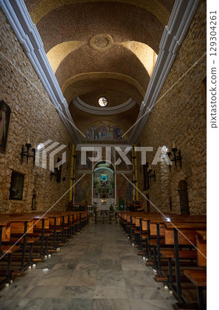 Interior of a Historic Stone Church Featuring Wooden Benches, Religious Artwork, and Natural Light 129304261
