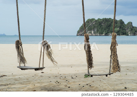 Couple of wooden swings on the beach with blurred seascape and island in background Couple of wooden swings on the beach with blurred seascape and island in background 129304485