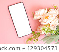 Smartphone with blank white screen placed on pink background beside pastel flowers. 129304571